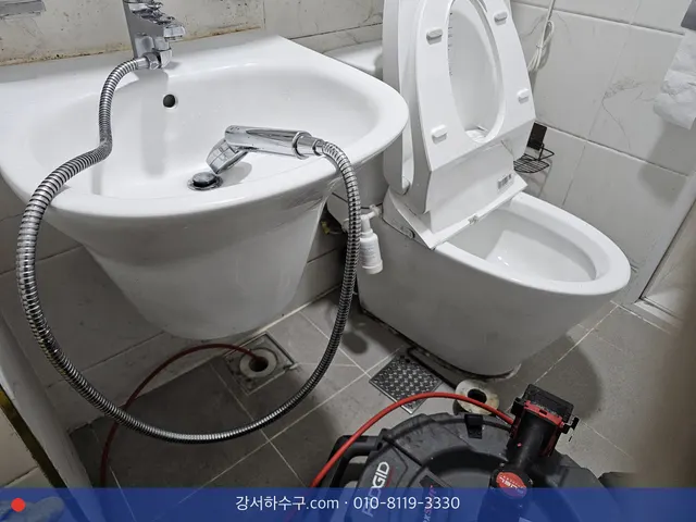 세면대와 변기 사이 바닥 배수구에서 작업 중인 스프링 기계