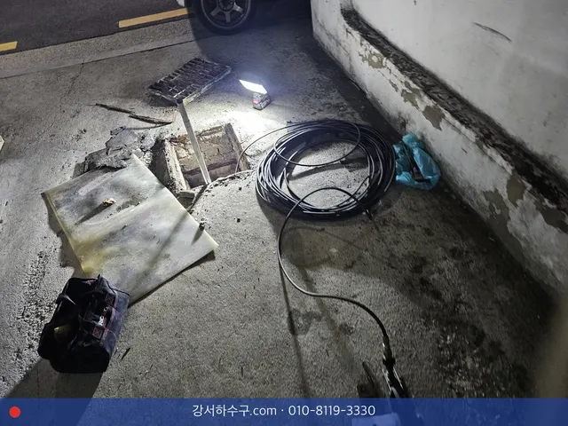 주차장 바닥 배수로 덮개를 열고 조명을 켠 채 작업하는 장면